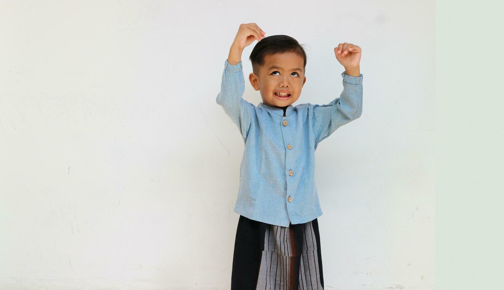 An adorable and cute little boy making a funny face while raising his hand gesture to playing something. Boy growth photo