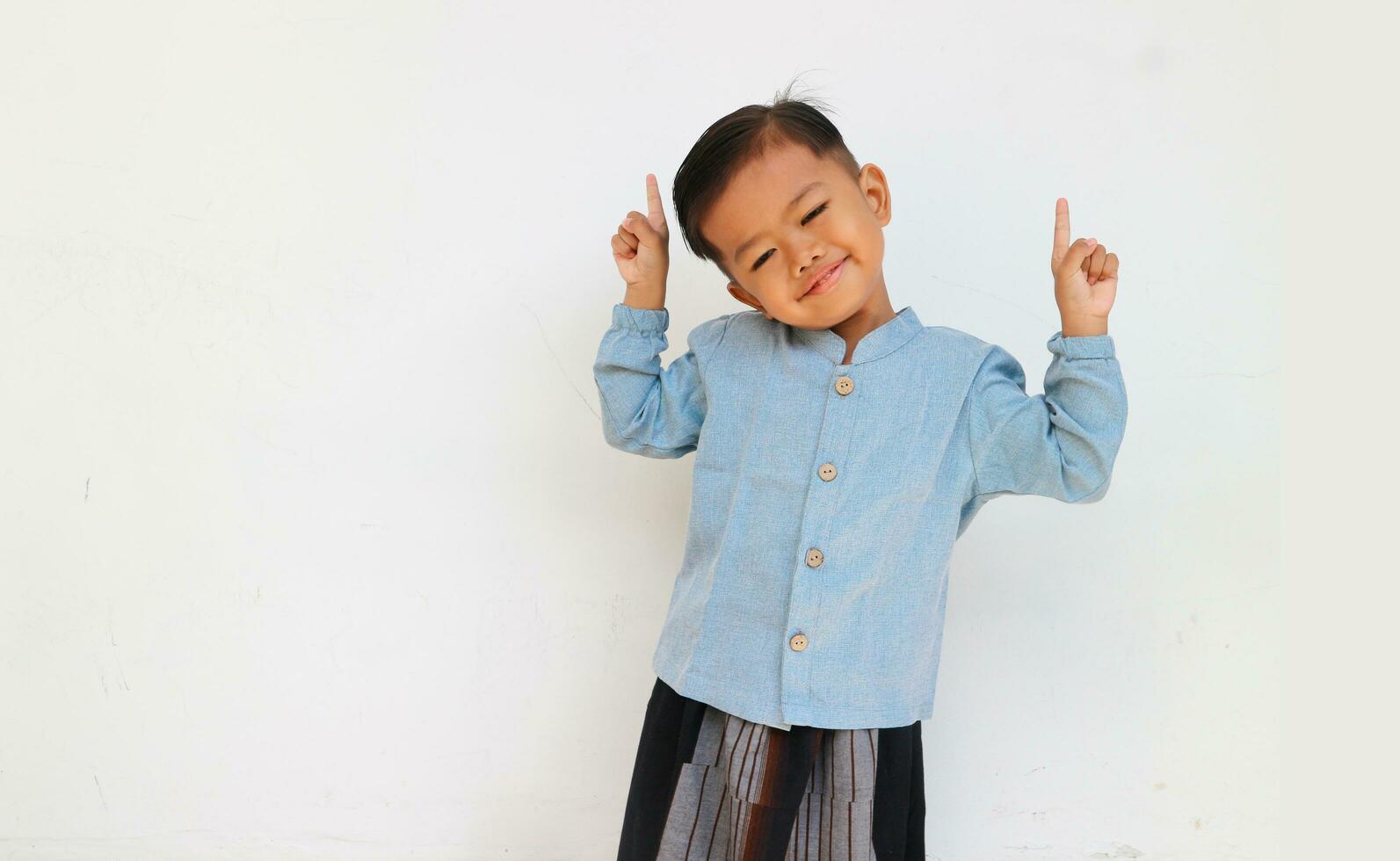 A smiling little boy closed his eyes while raising his hand and pointing up photo