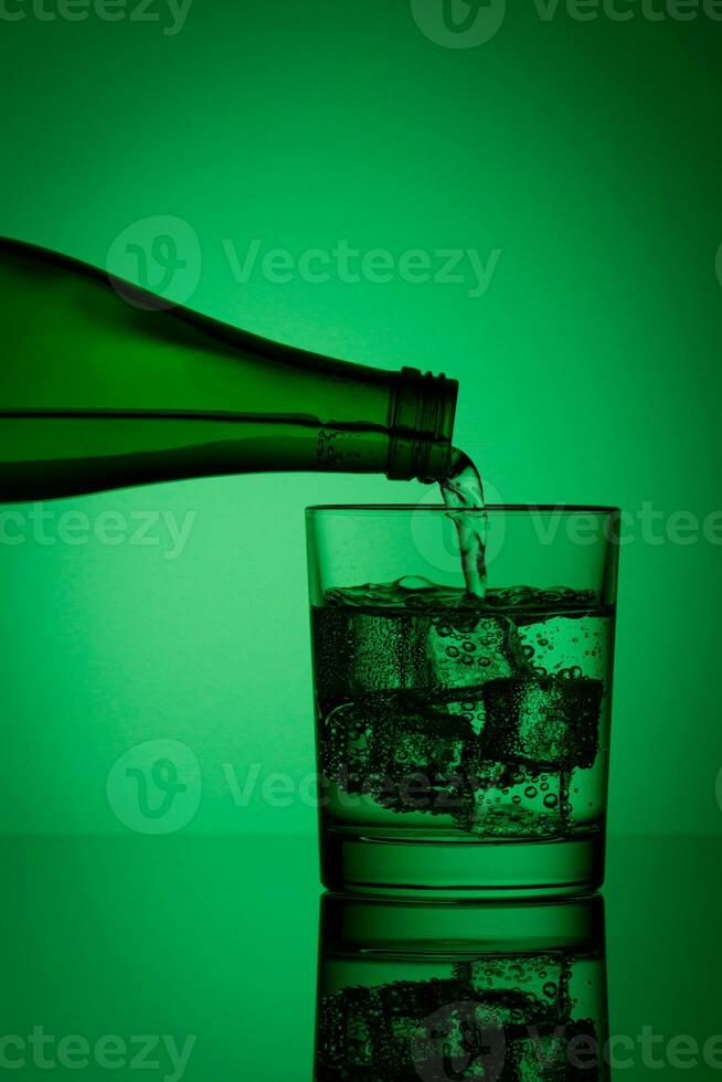 beautiful bottle with water and glass with ice and water on a green background photo