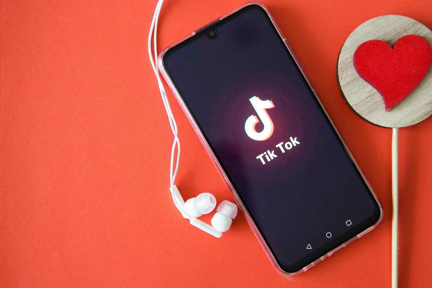 Tver, Russia-April 9, 2020, the tik tok logo on the smartphone screen on a red background with headphones. Tick-Tok icon. logo of the current app. Tiktok social network. photo