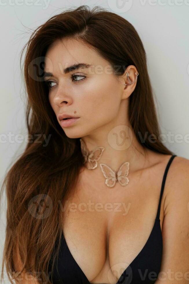 Close up portrait of seductive bunette woman  posing over white wall. Healthy long hairs. Fashionable necklase. photo