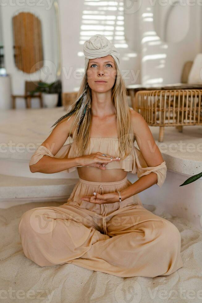 Stylish  blond woman with turban  in  indie bohemian style clothes .Boho woman  with long hair practising yoga asanas. photo