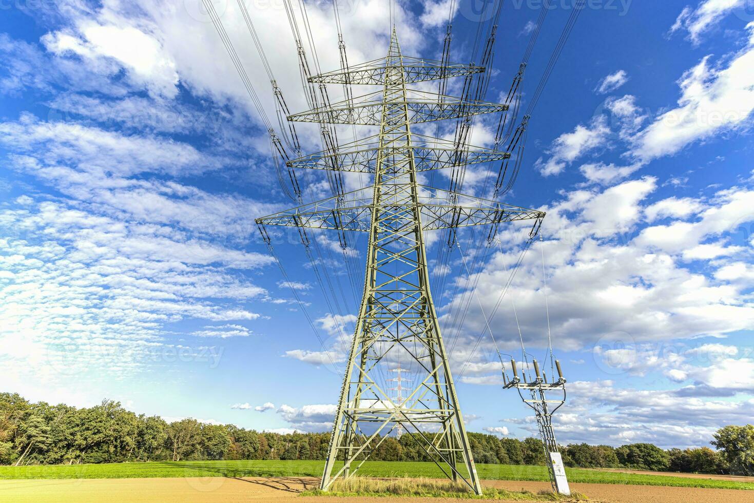 Image of an electricity pylon from the ground perspective in front of a blue sky with white clouds photo