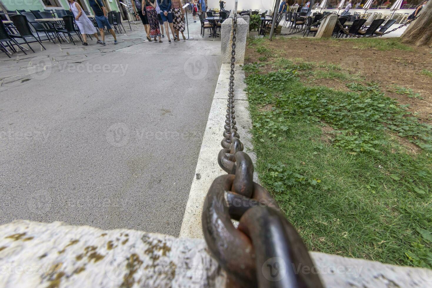 Picture along an iron chain that acts as a partition between the footpath and a green area photo