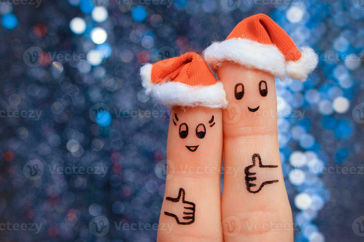 Finger art of couple celebrates Christmas. Concept of man and woman laughing in new year hats. Happy pair showing thumbs up. Toned image. photo