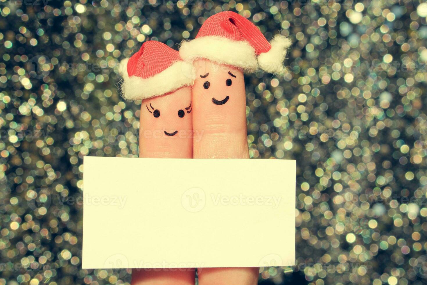 Finger art of couple celebrates Christmas. Concept of man and woman laughing in new year hats. Happy pair showing white blank page. Toned image. photo