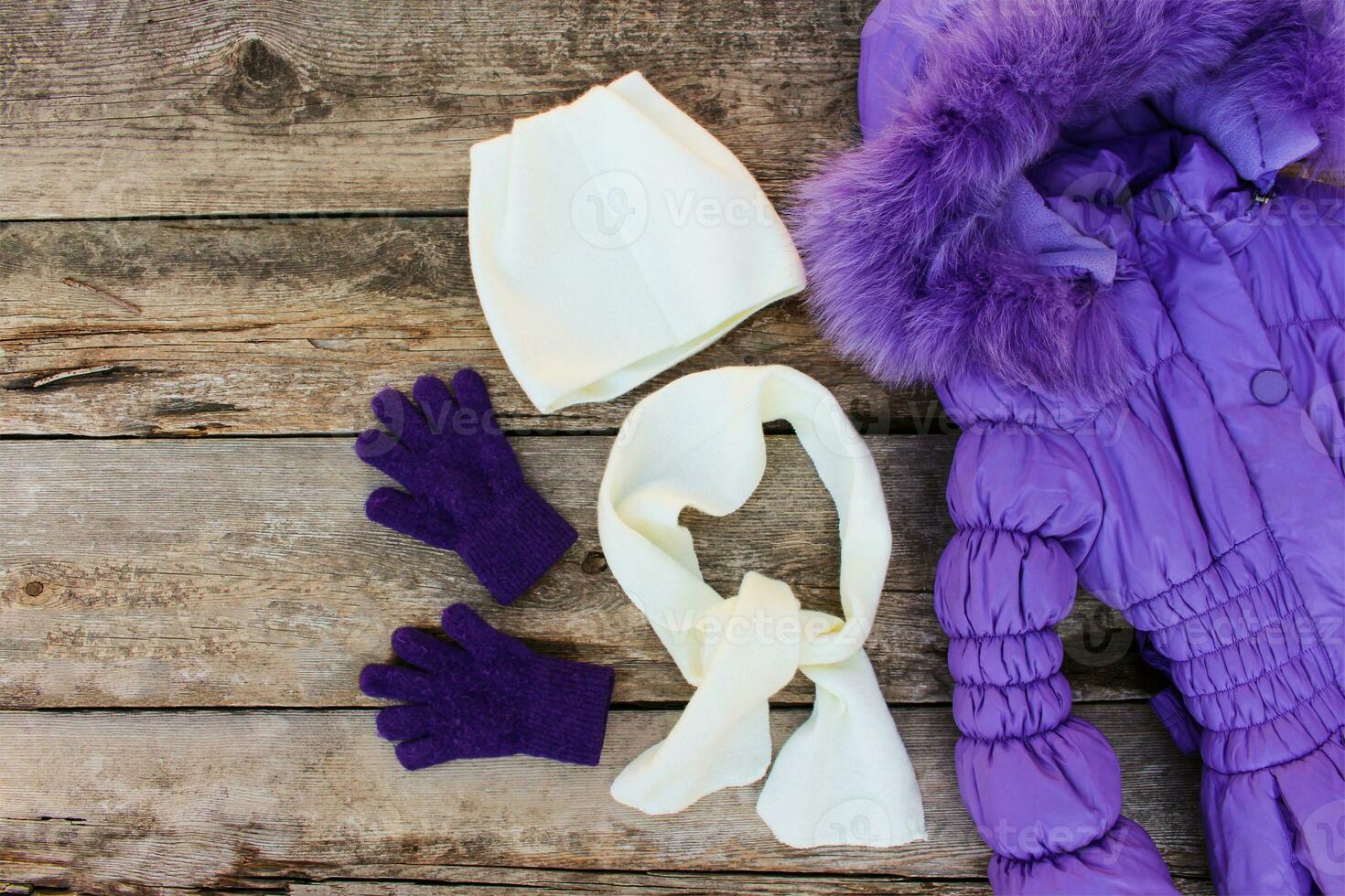 Children's winter clothes warm jacket, hat, scarf, gloves on old wooden background. Top view. photo