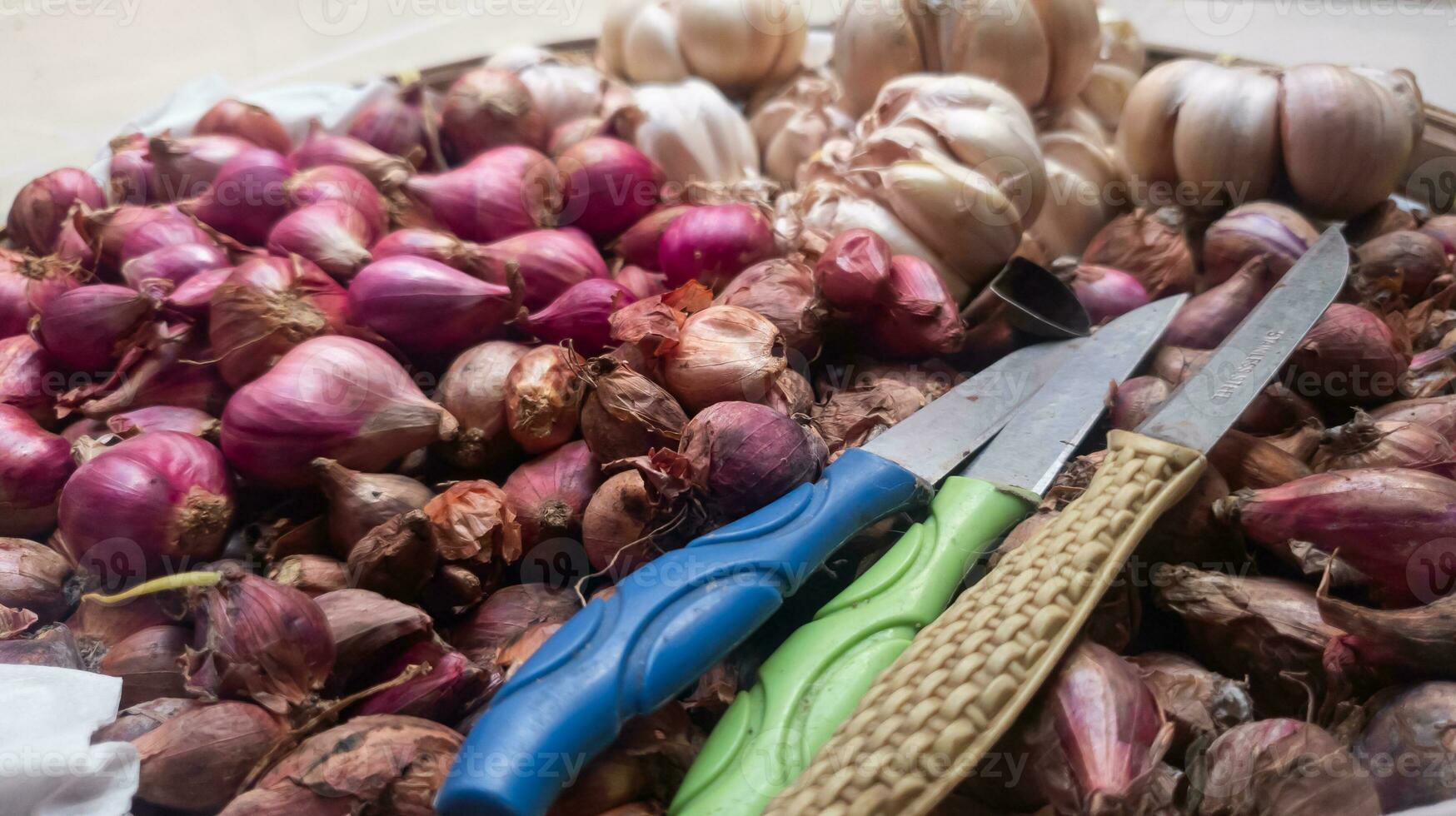 A bunch of red and white onions in a basket with a small knife on top photo