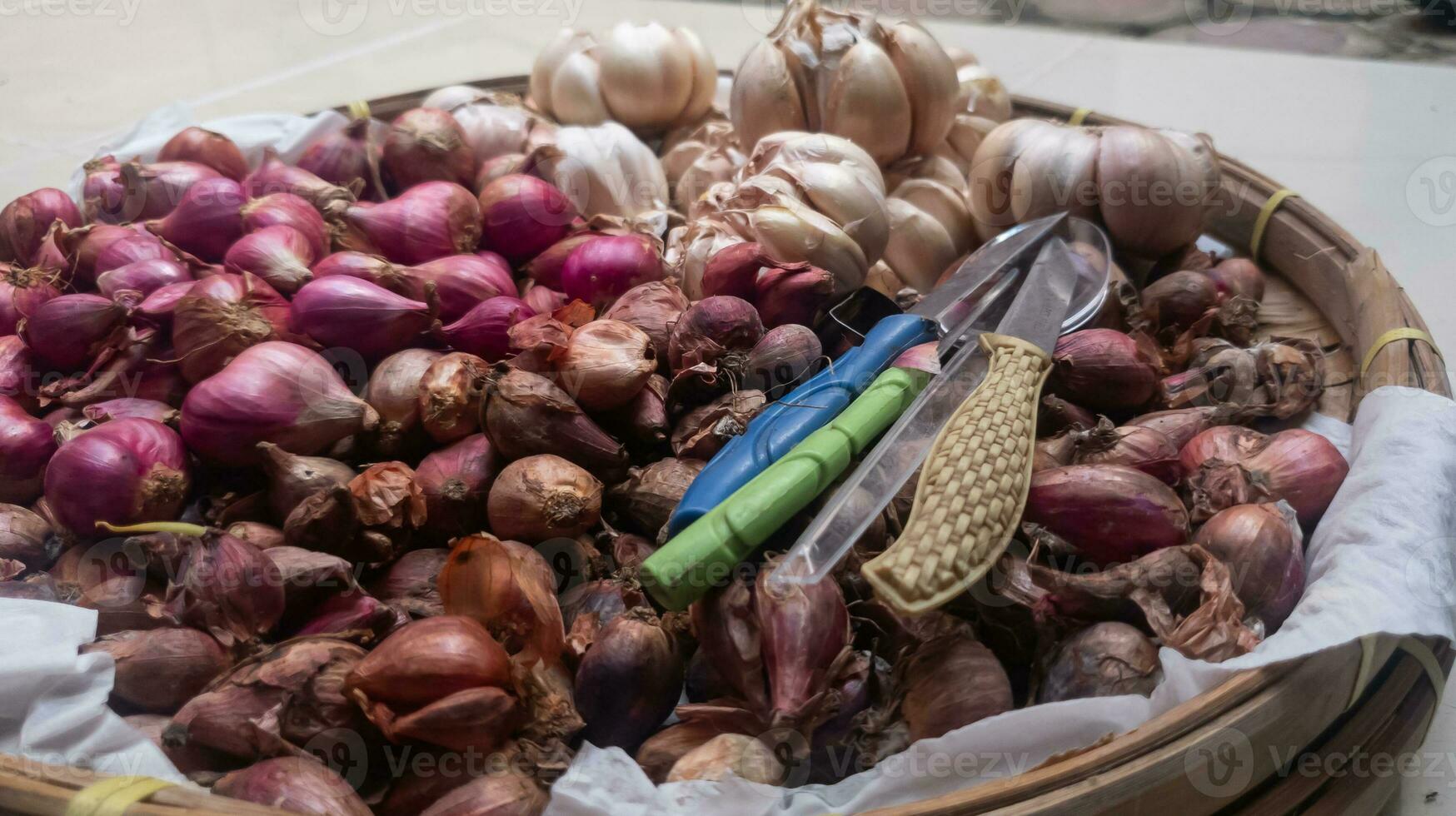 A bunch of red and white onions in a basket with a small knife on top photo