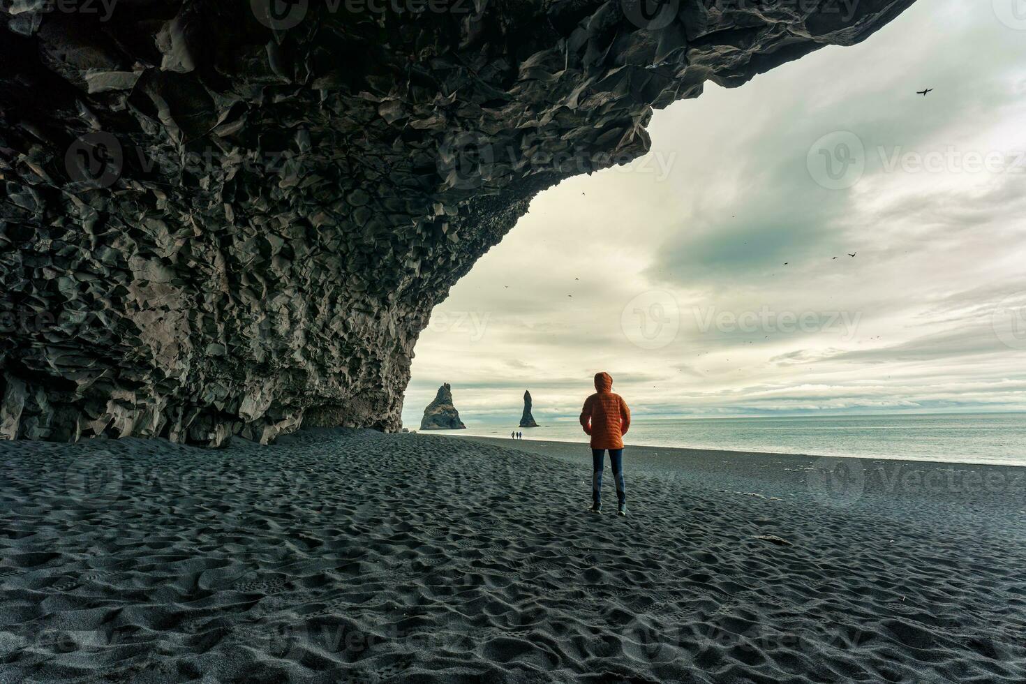Reynisdrangar natural rock formation with female tourist standing in halsanefshellir cave on black sand beach in summer at Iceland photo