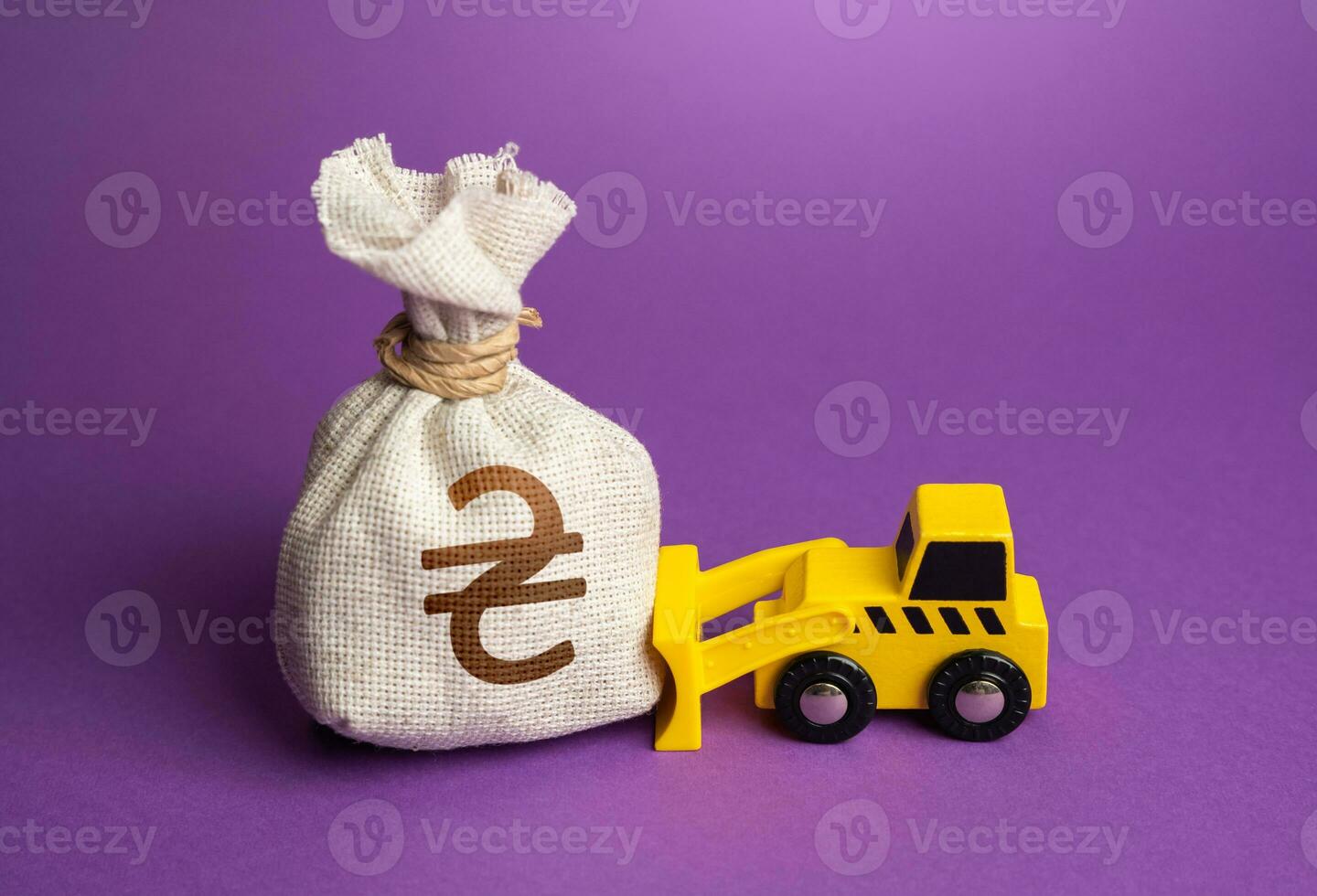 A bulldozer pushes a ukrainian hryvnia money bag. Financing of dismantling works. Demolition services, land leveling. Industry machinery for rent. Money down the drain. Ineffective use of funds. photo