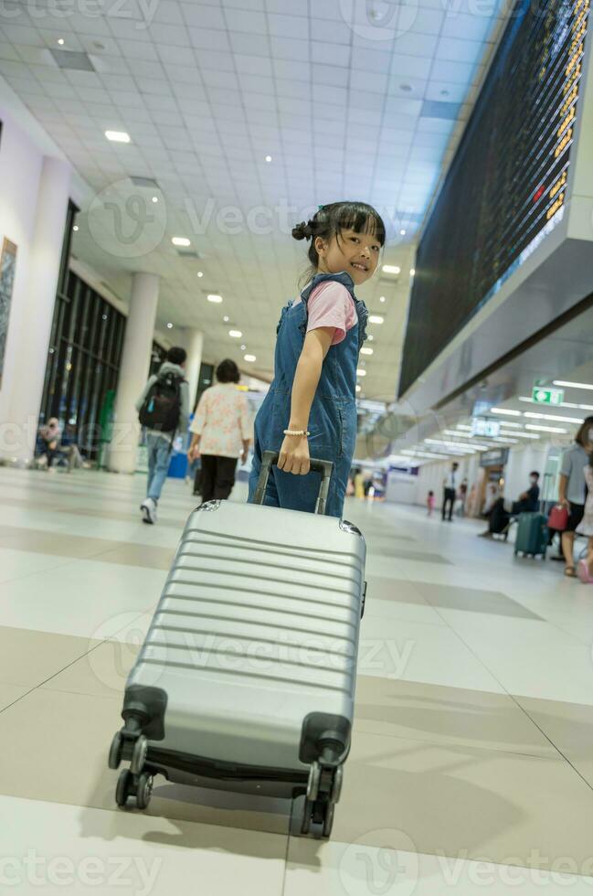 Cute happy child girl with suitcase at airport terminal. Kid and family traveling vacation for waiting boarding in terminal. Family travel concept. photo