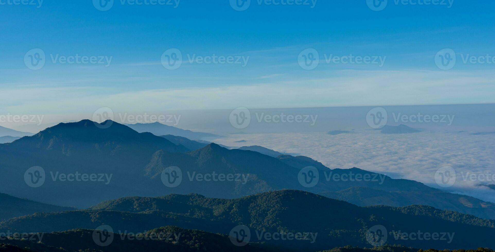 Mountain view in morning with blue sky background. countryside landscape with valley in fog behind the forest on the hill. nature background. photo