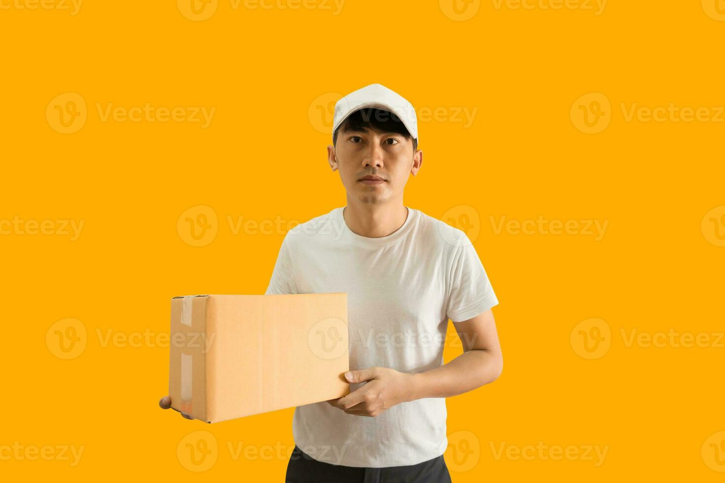 joven asiático entrega hombre vistiendo gorra y blanco blanco camiseta participación paquete o empaquetar enviar caja aislado en amarillo antecedentes. Rápido entrega Servicio concepto. foto