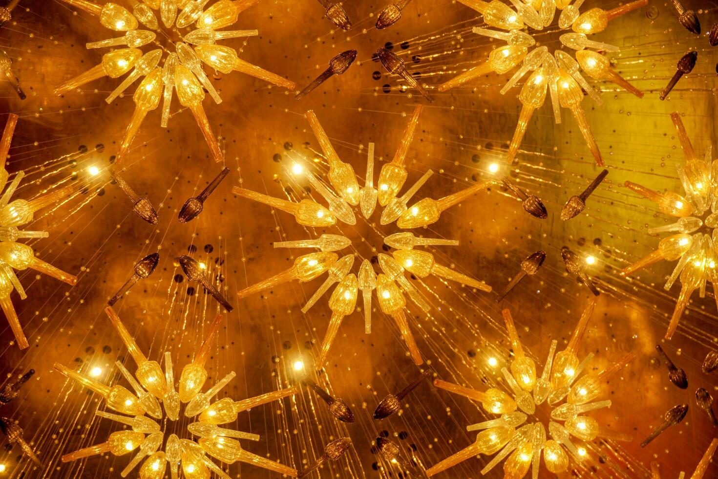 Look up view of modern and decorate chandelier hang on hall's ceiling with bright golden yellow lights. photo