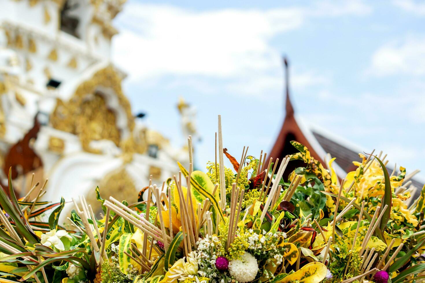 Closeup and crops heap of fragrant flowers with incense for worship the Buddha on blurry Thai temple sanctuary and blue background. photo