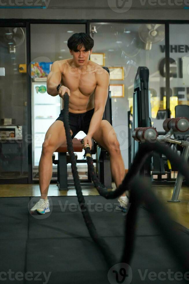 Closeup Asian handsome man workout training the battle rope in fitness center. photo