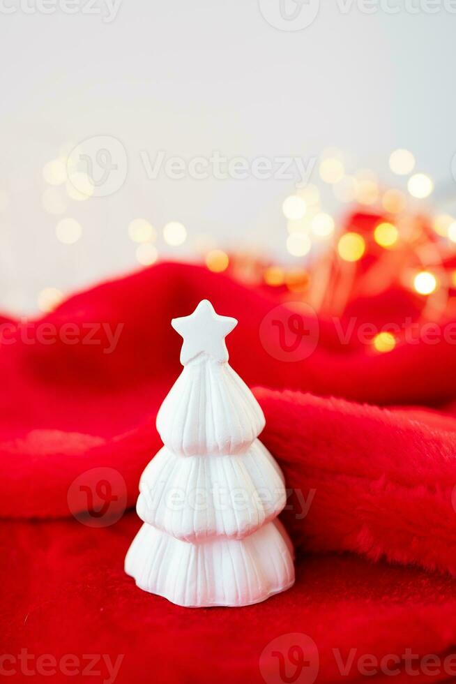 Christmas home interior with a white ceramic Christmas tree on a red blanket. Christmas and New Year concept. Vertical photo. photo