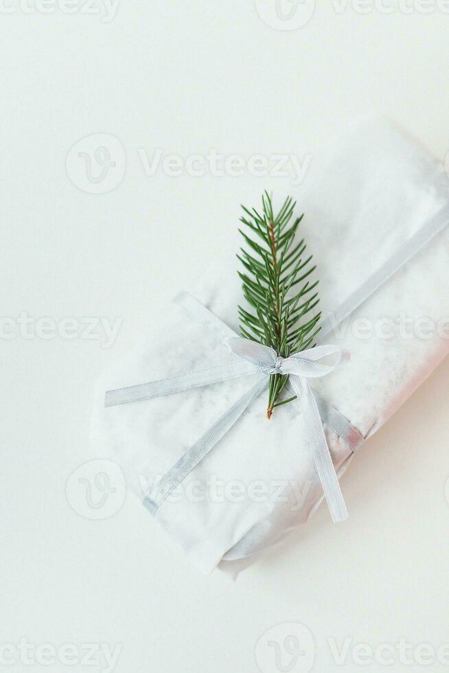 A homemade Christmas stollen sealed in white craft paper, along with a sprig of a Christmas tree, lies on a white background. Gift wrap. photo