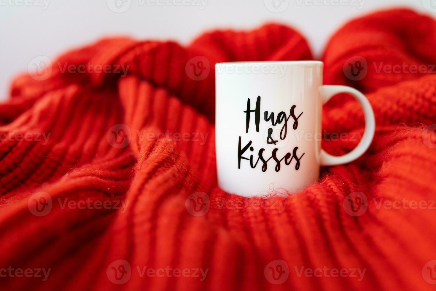 A white cup with a heart stands on a red knitted fabric. Inscription of St. Valentine's day, 14 February. photo