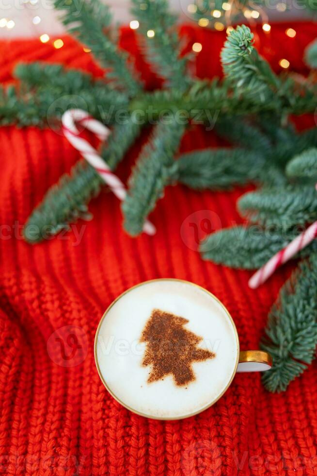 Navidad composición hecho de noruego nobilis pino y decorado con luces y caramelo bastones en el formar de un caña. un taza de capuchino con un Navidad árbol modelo. Navidad y nuevo año concepto. foto