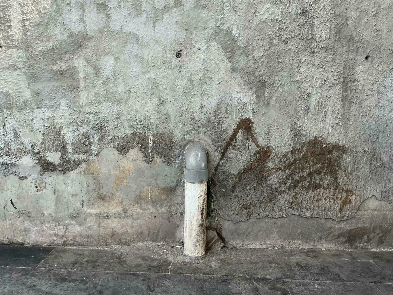 Unclean concrete wall outdoor with grungy textured stain isolated on horizontal ratio and water pipe going down to the ground object. photo