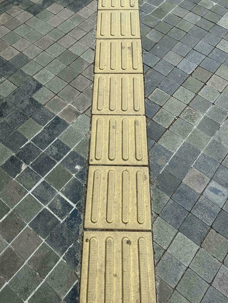 Braille pavement straight lines yellow blocks squares isolated on concrete stone flooring background outdoor. Guide for blind people on public side walk street. photo