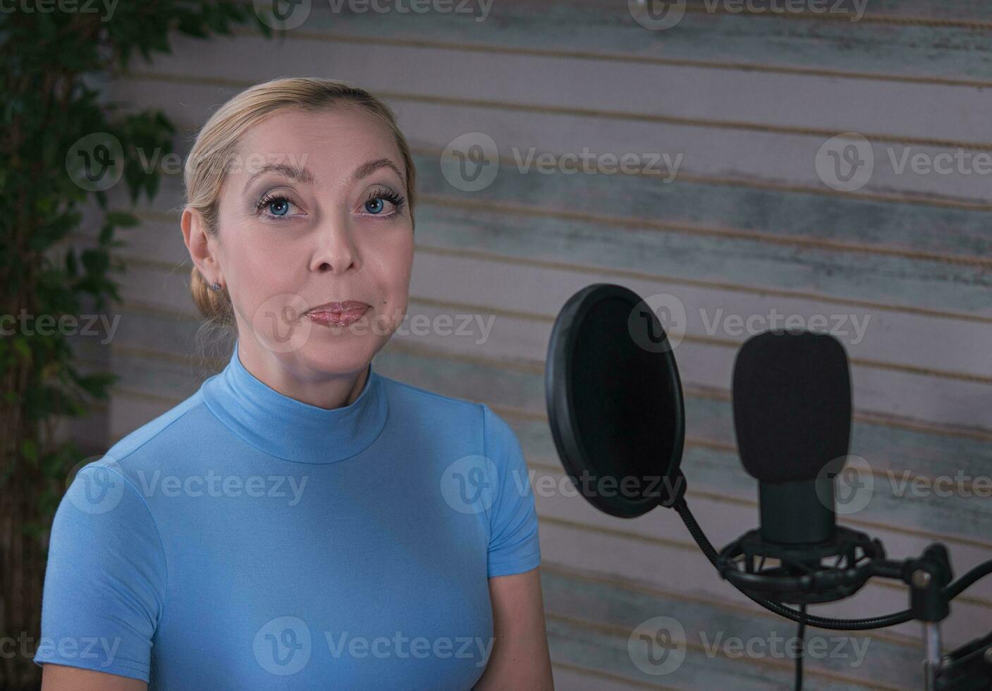 A beautiful blonde woman hosts a podcast against the backdrop of a large ficus tree photo