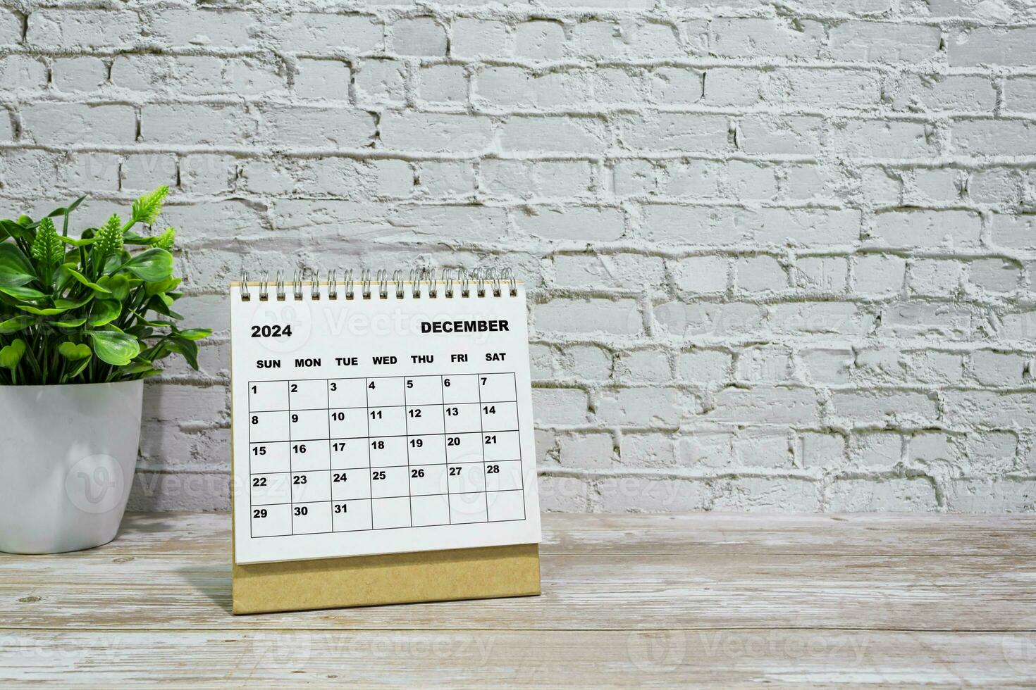 White December 2024 calendar on office wooden desk with potted plant. photo