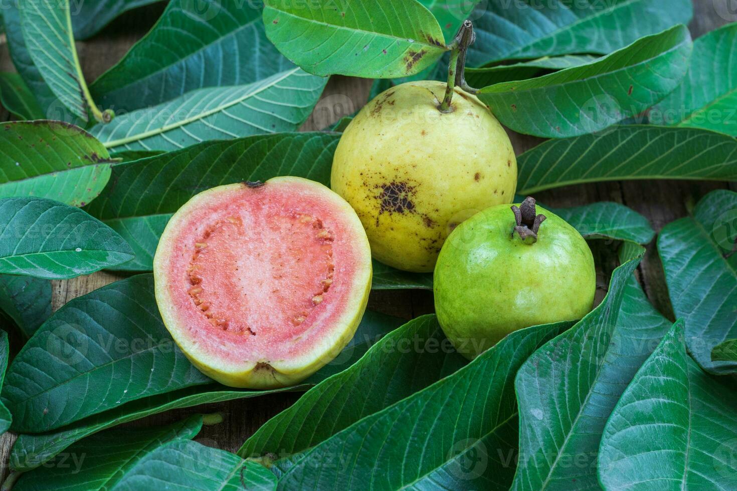 Fresh red guava with green leaves on wooden background. Texture of wood and guava leaves. photo