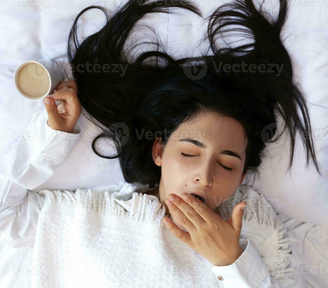 Beauty woman drinking coffee in bed after waking up in morning. Young beautiful woman in bed with cup of coffee. Cute lady waking up. Breakfast in a cozy bedroom photo