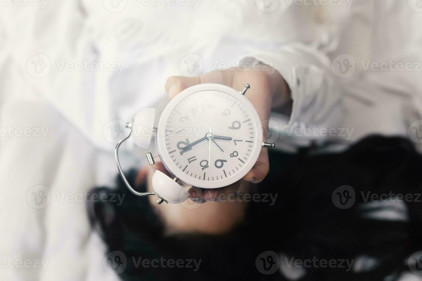 Good morning. Happy woman in bed waking up and holding up an alarm clock. Waking up at 7 a.m. early morning. Shiny and sunny morning photo