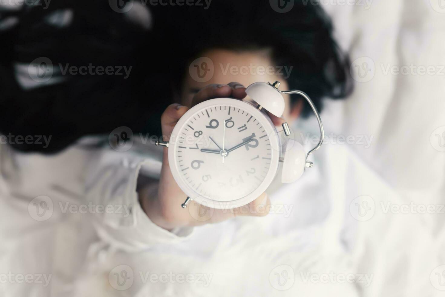 Good morning. Happy woman in bed waking up and holding up an alarm clock. Waking up at 7 a.m. early morning. Shiny and sunny morning photo