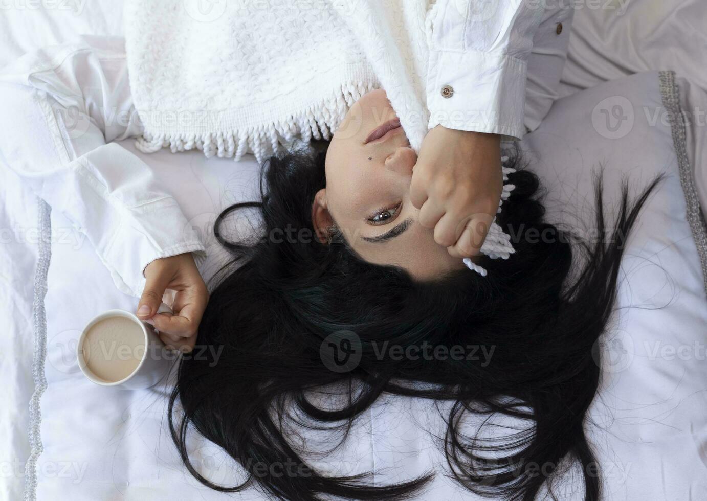belleza mujer despertar arriba en Mañana y Bebiendo café en cama. joven hermosa mujer en cama ocultación su cara con tartán y participación taza de café. linda dama despertar arriba. desayuno en un acogedor dormitorio foto