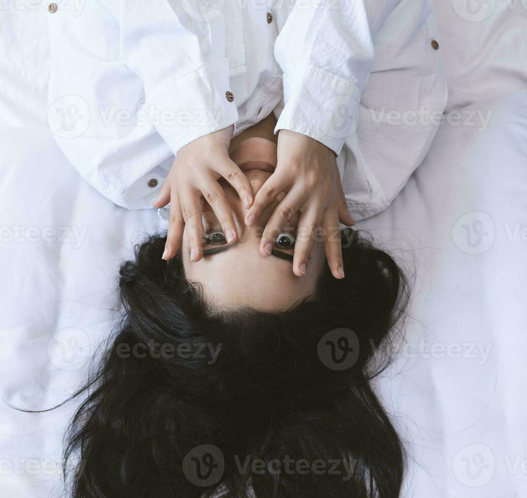 Beautiful woman lying in bed. Sexy black haired lady posing with her finger in mouth. Female enjoying, biting finger. Feeling happy, recreation, satisfaction and enjoyment. photo