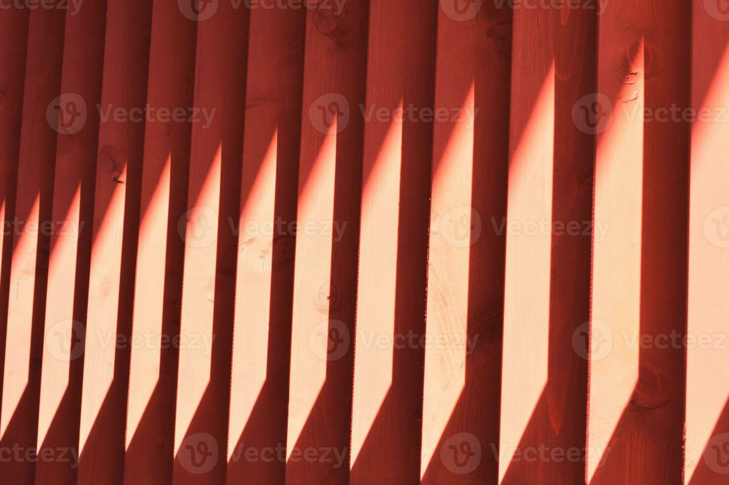 Red wooden slats. Abstract pattern with vertical lines and sunlight. Part of a bench, an element of building decor. photo