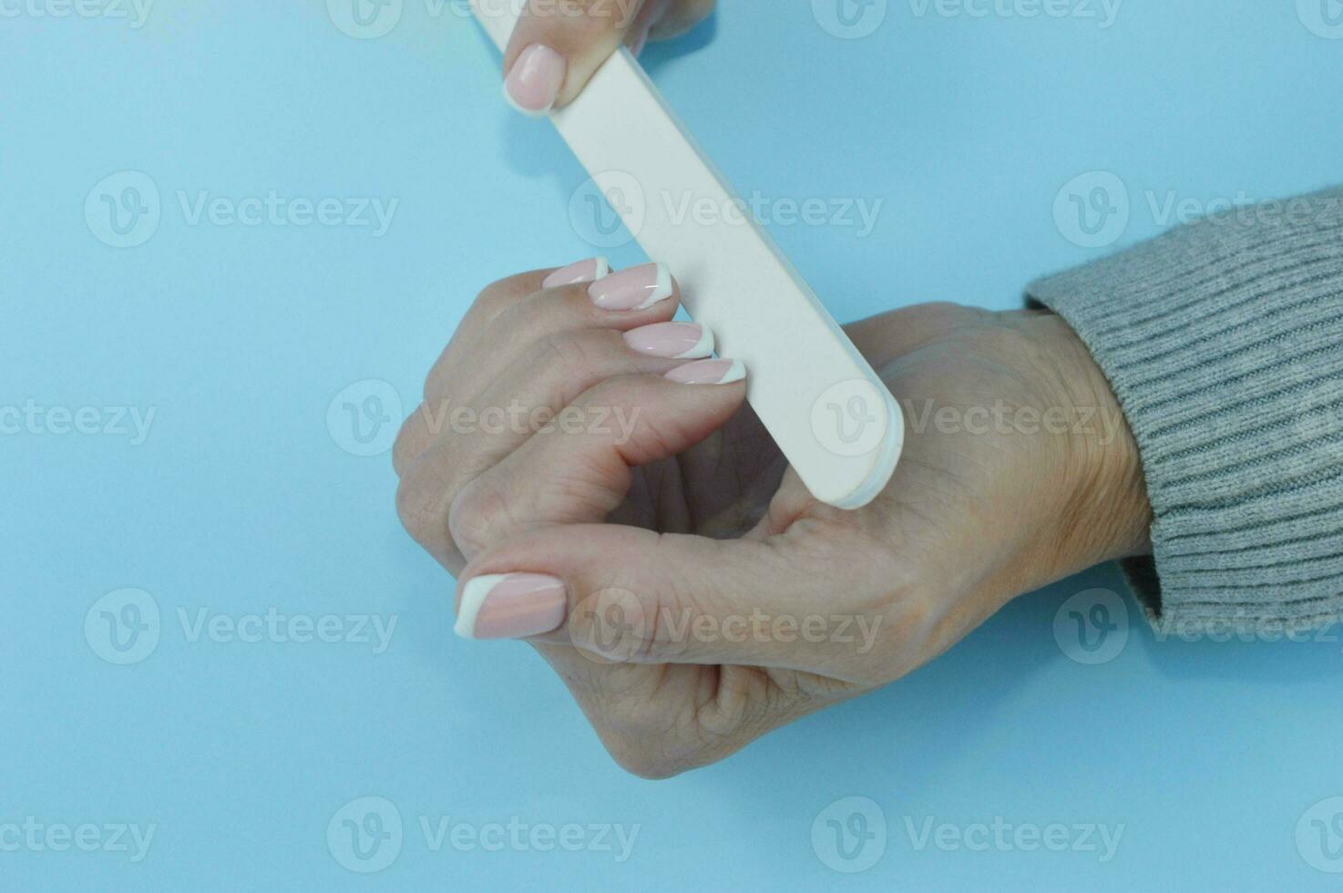 Female hands hold a nail file, filing nails with a beautiful manicure. photo