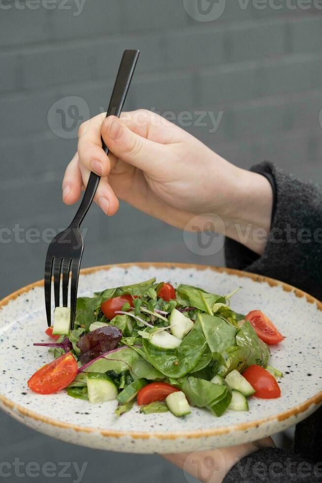 mujer comiendo Fresco ensalada con Rúcula, Cereza Tomates, pepinos en un lámina, de cerca foto