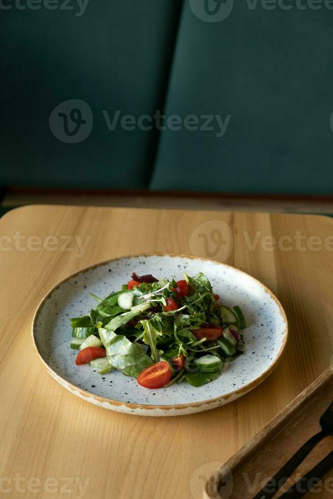 Fresh salad with arugula, cherry tomatoes, cucumbers in a plate against cafe interior photo