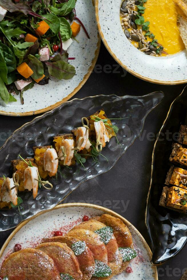 Sandwiches with shrimps and other dishes in plates on dark background. Delicious autumn dishes photo