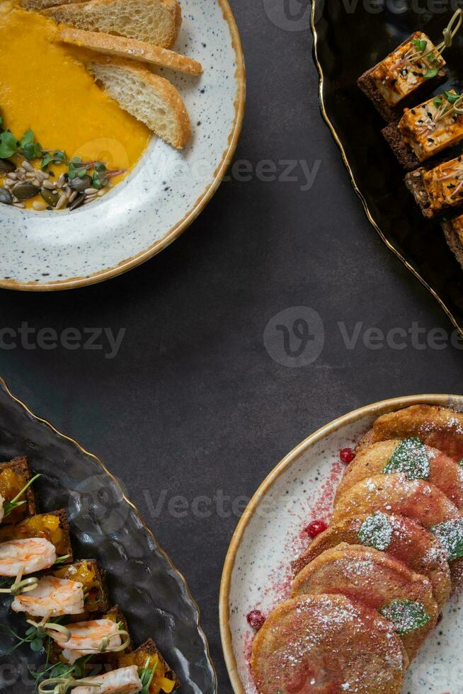Fragments of plates with different dishes on dark background with copy space top view. Delicious autumn dishes photo