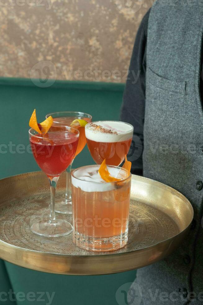 Four bright alcoholic cocktails on a tray in glasses in the hands of a bartender photo