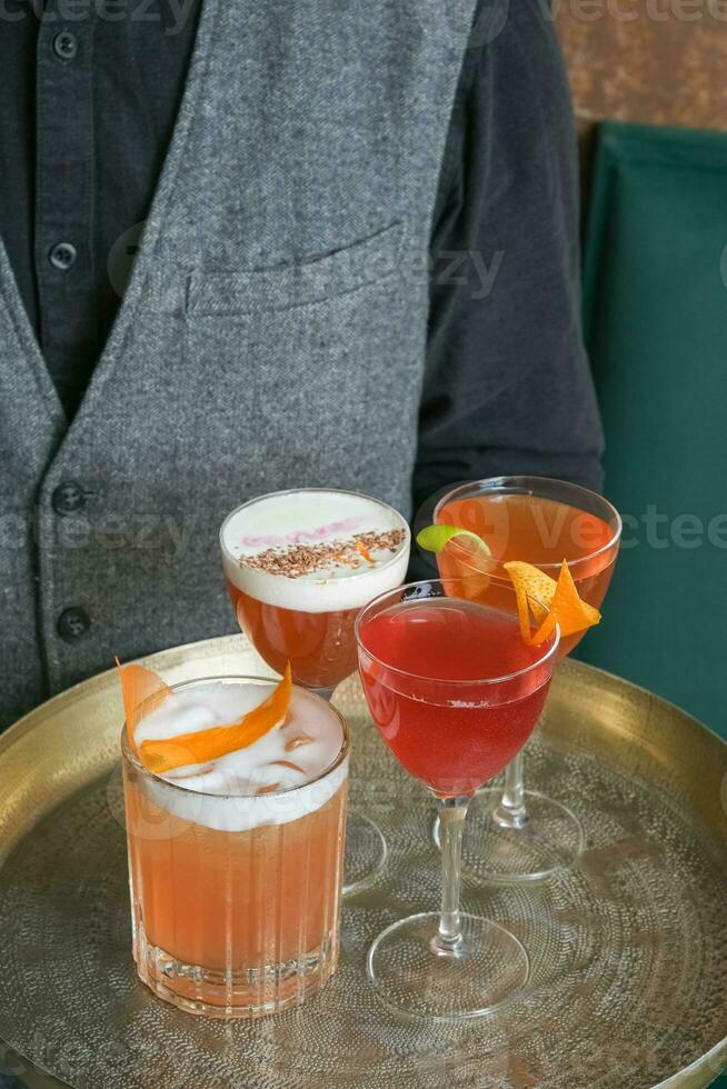Four bright alcoholic cocktails on a tray in glasses in the hands of a bartender photo