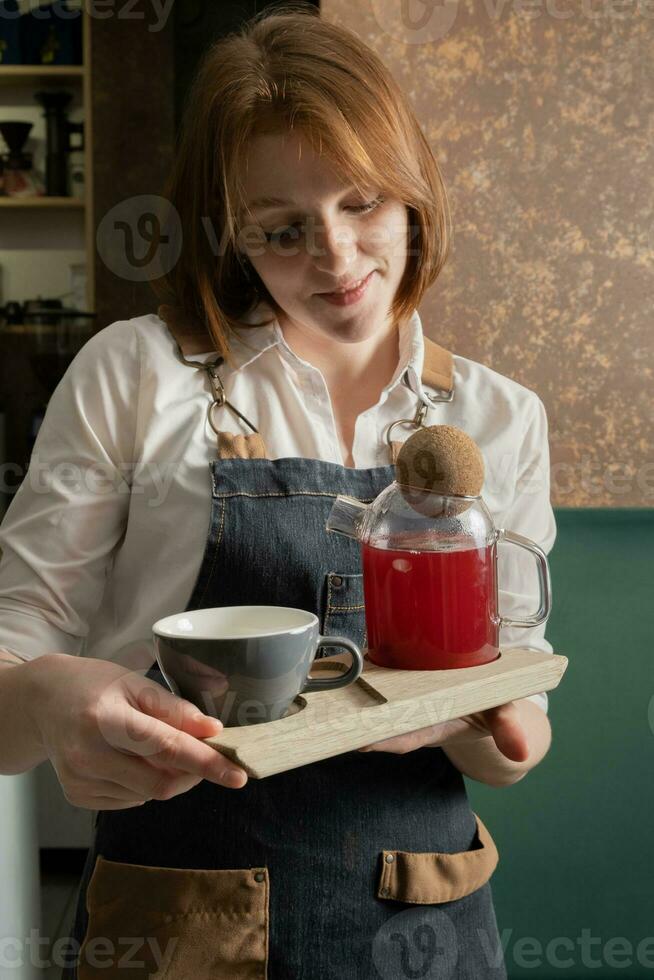 A cup and a teapot with cranberry tea in the hands of a waitress photo