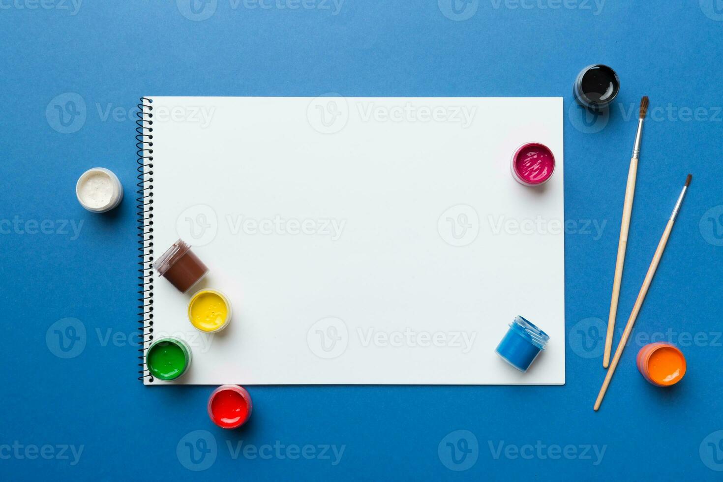 Album pages and paints, pencils, brush on a colored background. Top view with empty space. workplace for creativity. home teaching concept drawing photo