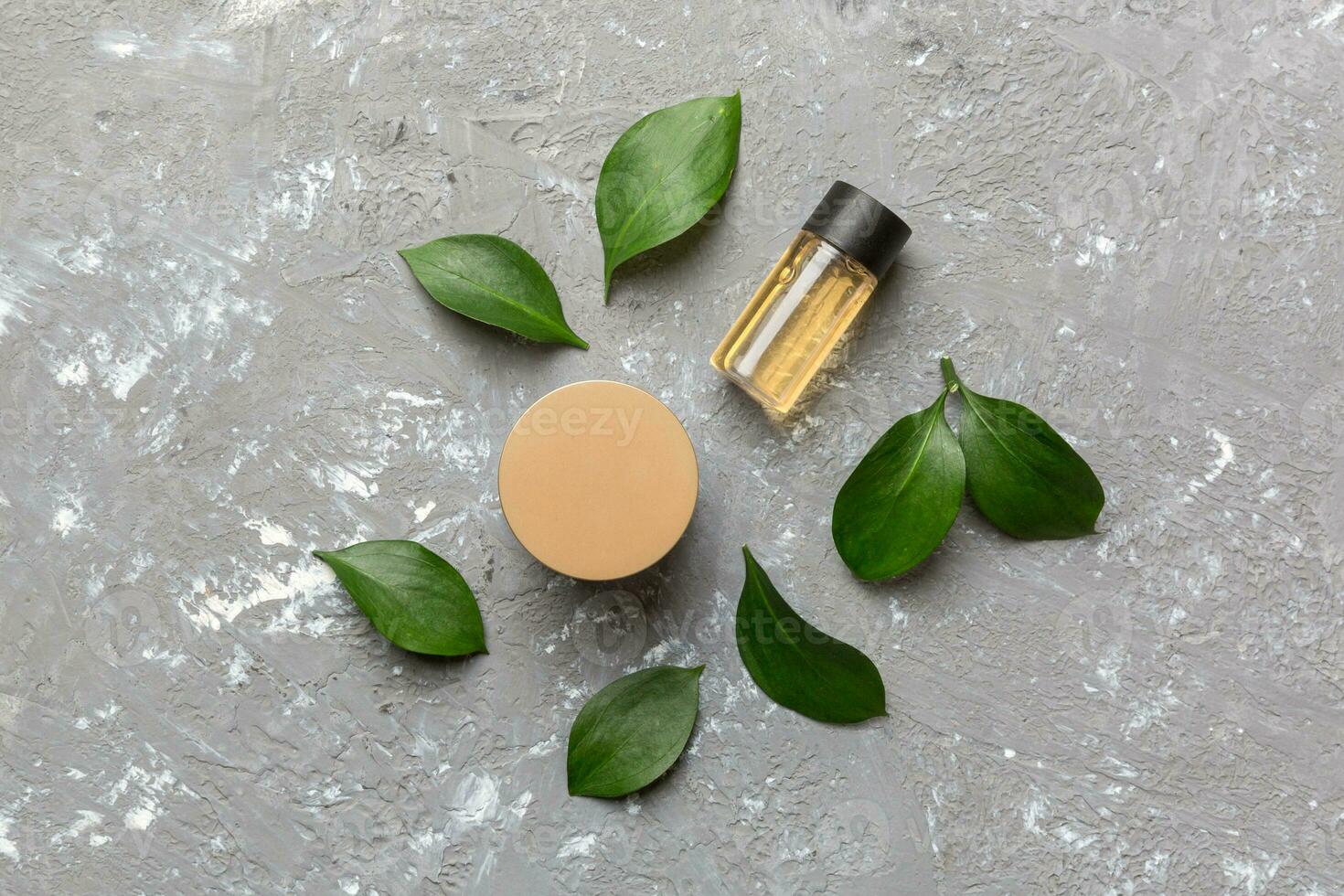 Organic cosmetic products with green leaves on cement background. Flat lay photo