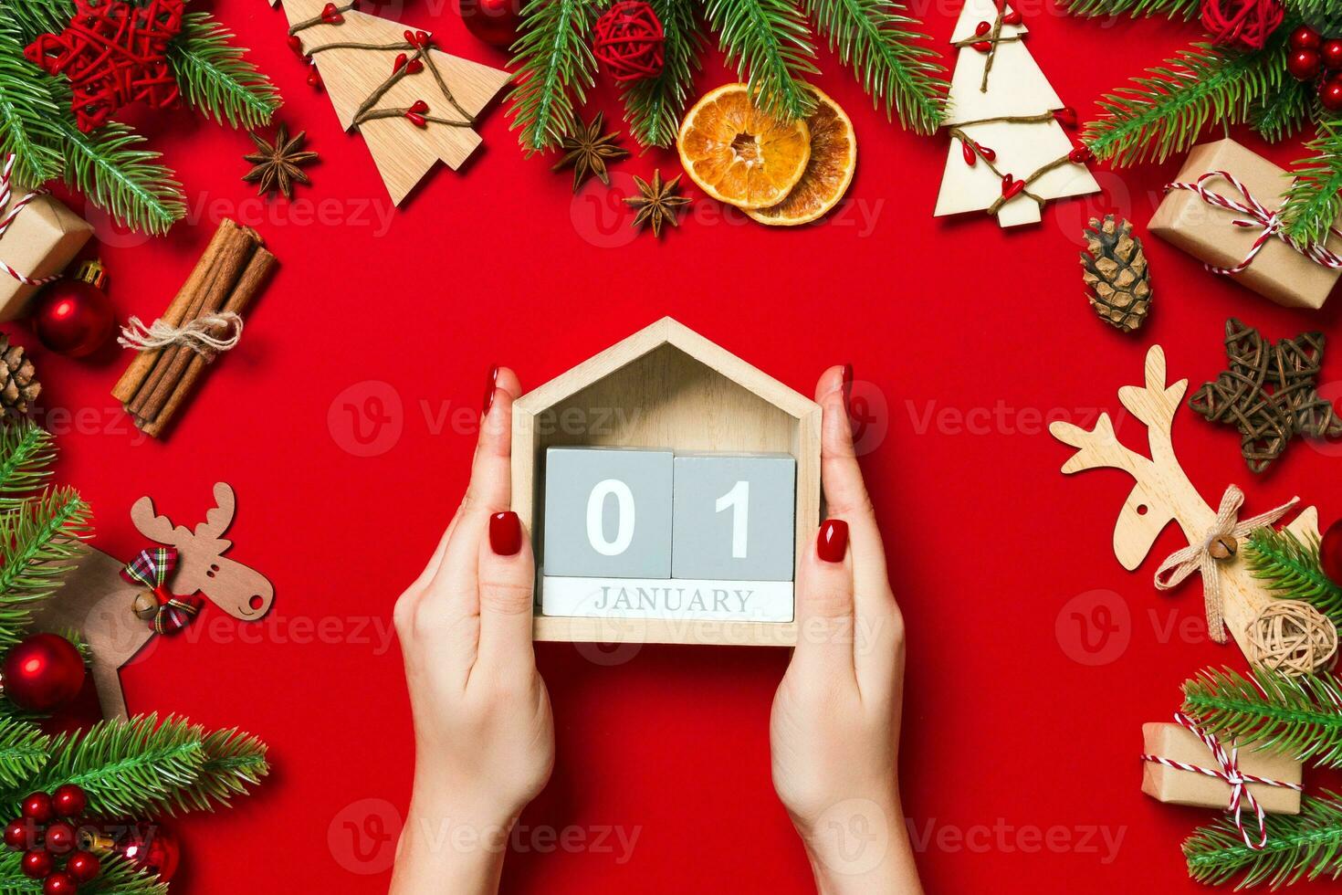 Top view of female hands holding calendar on red background. The first of January. Holiday decorations. New Year concept photo