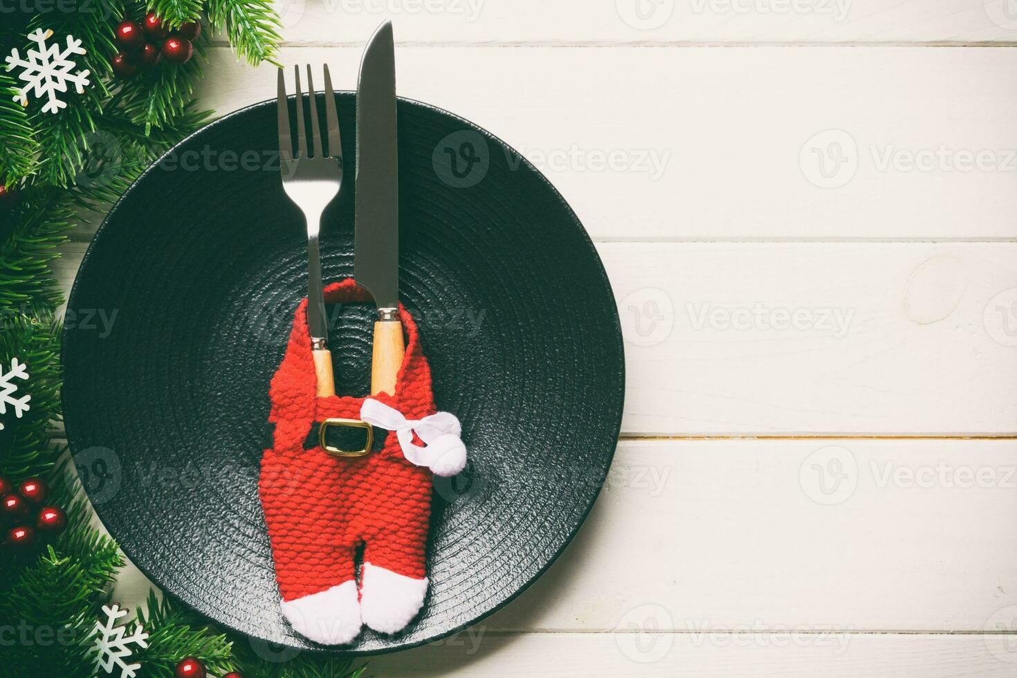 Top view of Christmas dinner on wooden background. Plate, utensil, fir tree and holiday decorations with copy space. New Year time concept photo