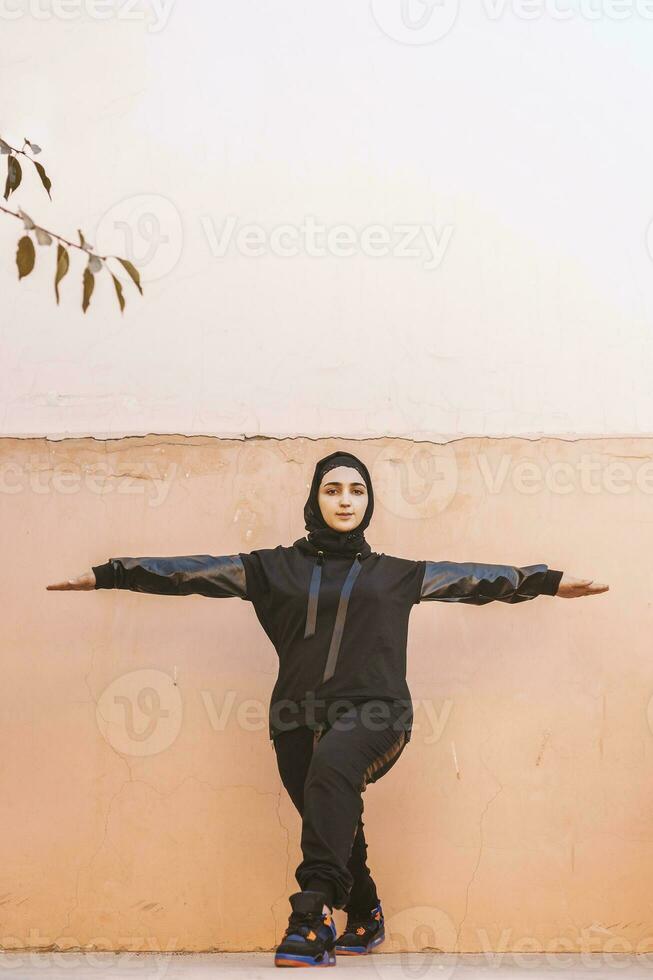 A Muslim woman does physical exercises. Middle-eastern woman in hijab training outdoors. Doing physical exercises on fresh air. Muslim female exercising outdoors in the morning photo
