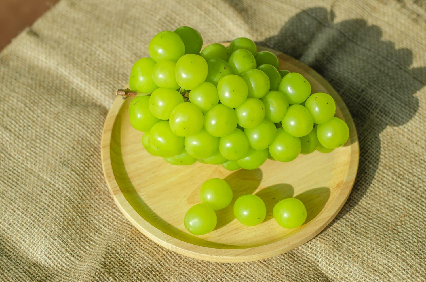 Bunches Shine Muscat grapes placed on wooden plate. Top view photo